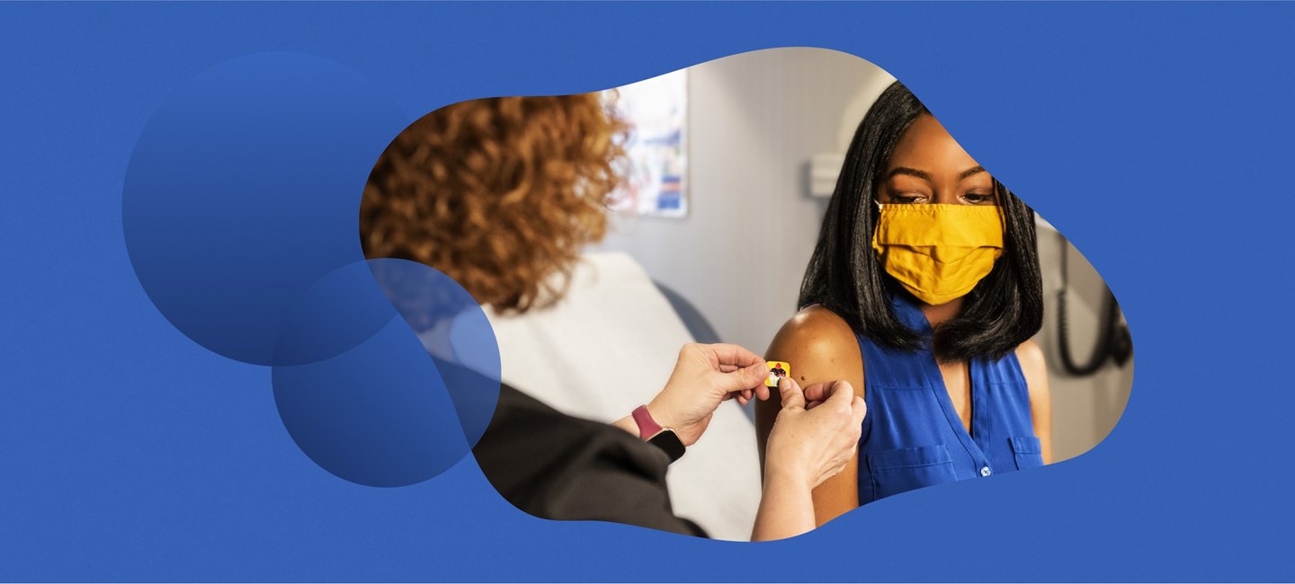Person putting a patch on the arm of a woman wearing a mask.